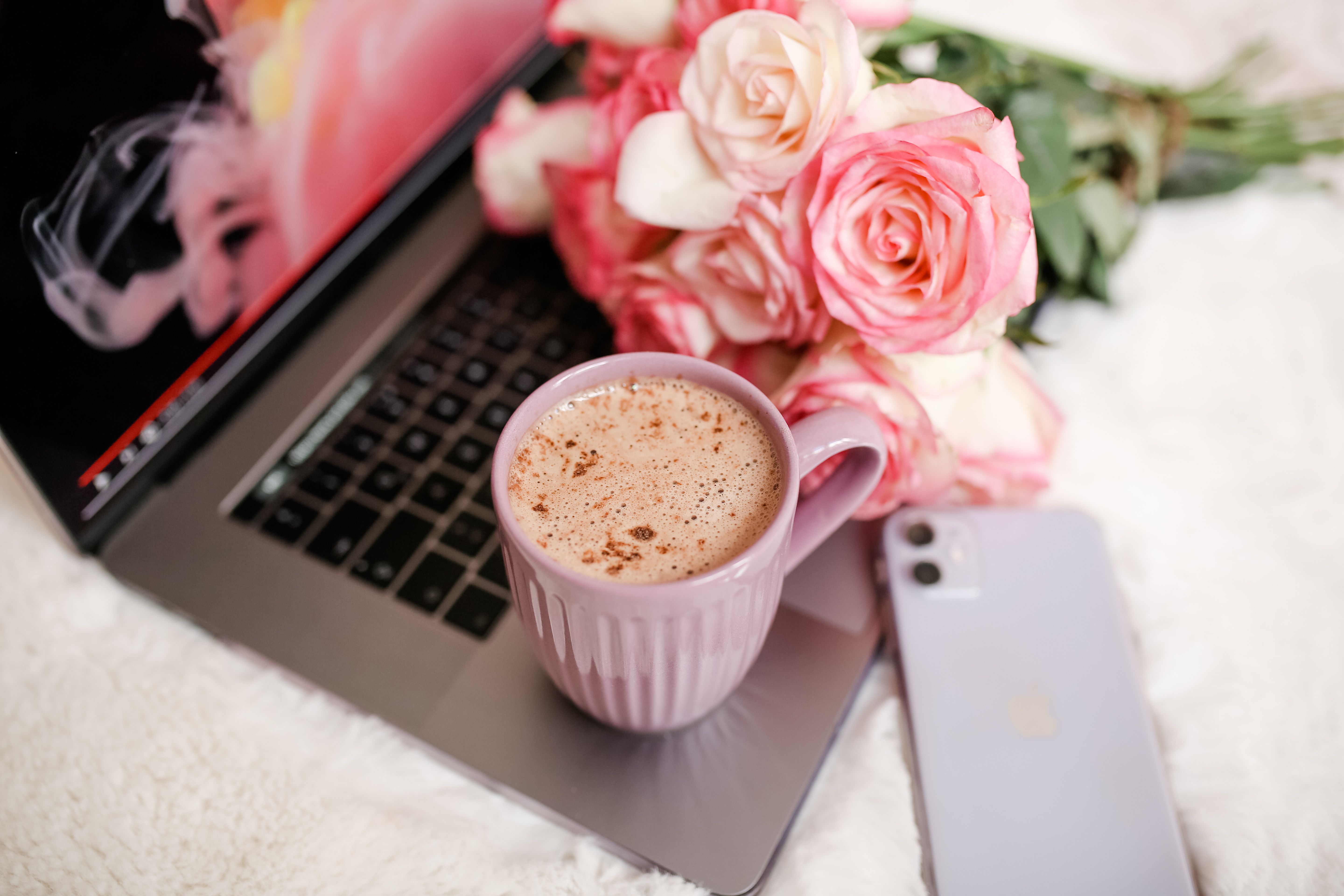 Laptop, celular e rosas sobre a mesa, representando o planejamento de um site de confirmação de presença para eventos