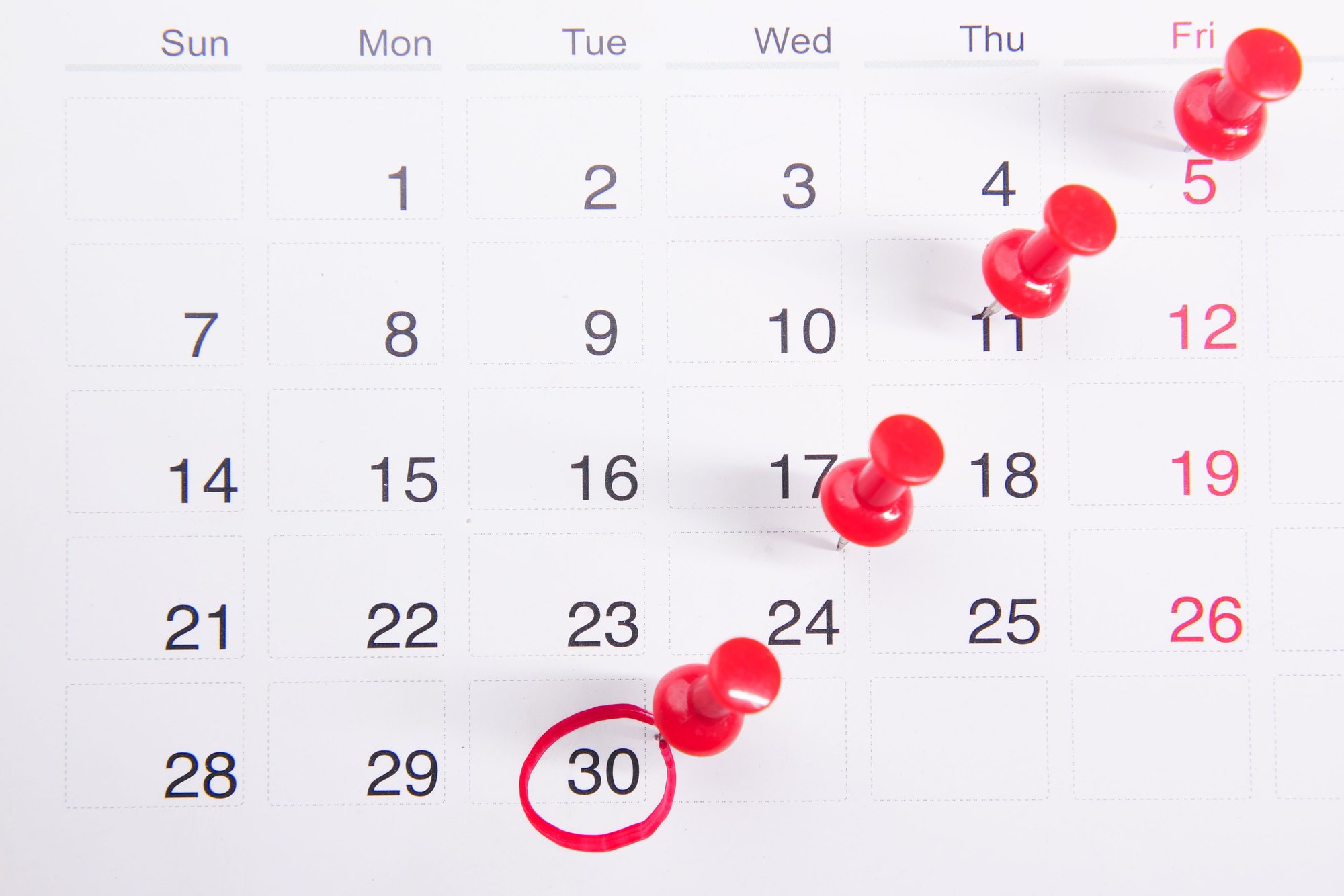 Calendário de mesa com vários pins vermelhos marcando datas diferentes, representando vários eventos ao mesmo tempo
