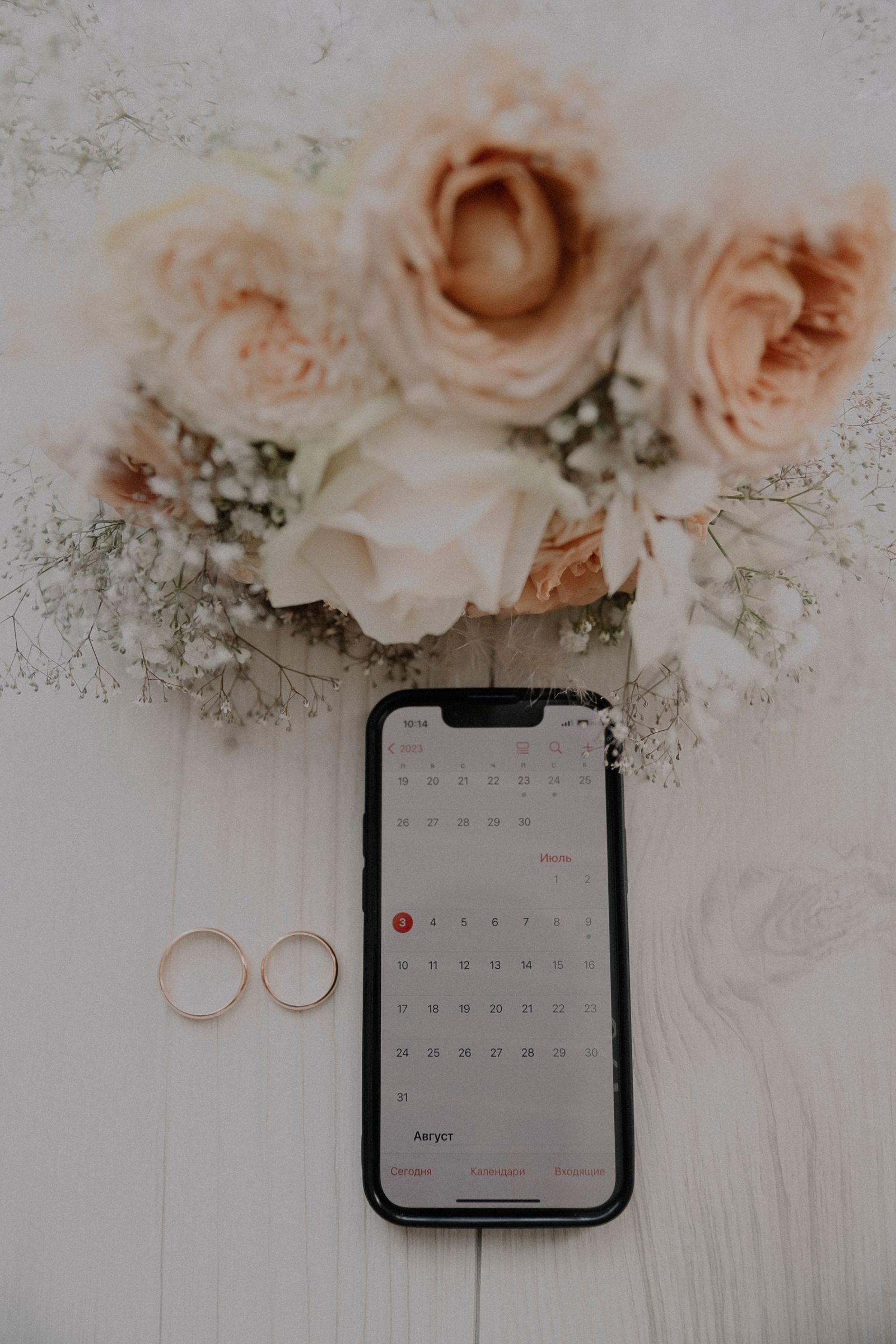 Buquê, alianças e smartphone mostrando data marcada no calendário, representando o convite e a confirmação de presença digitais