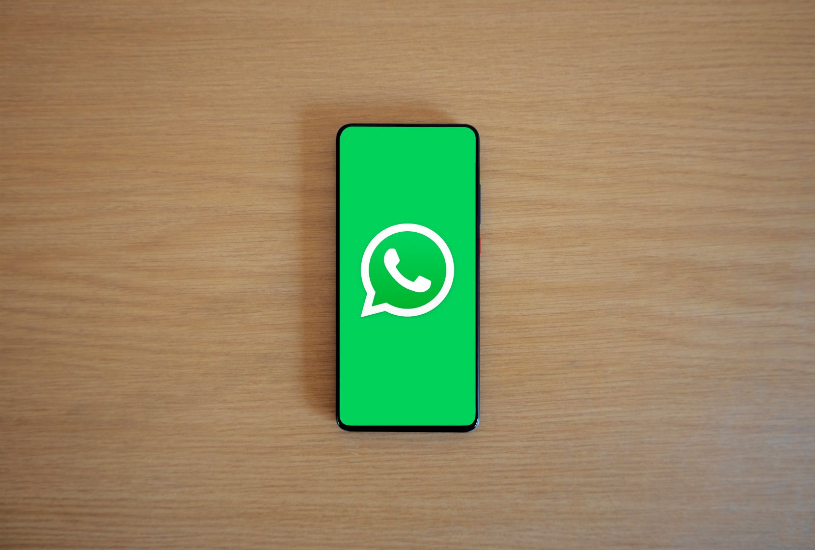 Ícone do WhatsApp em tela de smartphone sobre mesa de madeira, representando o RSVP via WhatsApp