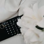 Celular com calendário aberto ao lado de sapato de noiva, alianças e buquê, simbolizando a escolha da data em alta temporada de casamentos