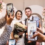 Noivos posando enquanto convidados registram o momento com celulares no casamento
