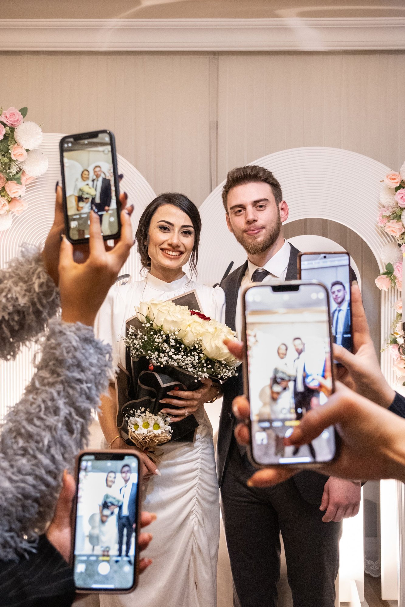 Noivos posando enquanto convidados registram o momento com celulares no casamento