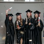 Formandas comemorando a formatura com beca, capelo e diploma nas mãos