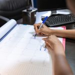Profissional de eventos marcando prazo de confirmação de presença em calendário de mesa